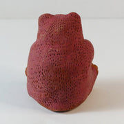 Small sculpture of a brown bear, chubby and sitting on its bottom. It has a red coloring for the top half of its body.