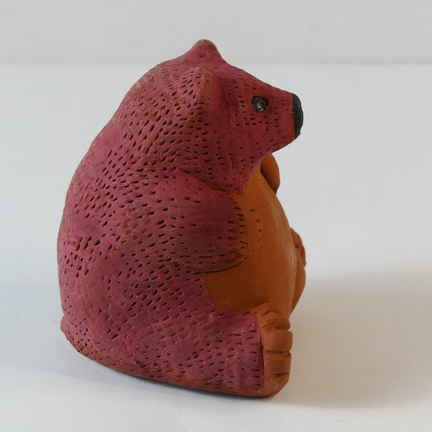 Small sculpture of a brown bear, chubby and sitting on its bottom. It has a red coloring for the top half of its body.