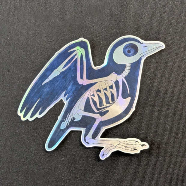 A die-cut sticker of a black bird (maybe a small crow) that looks like it's being run through an X-ray machine. metallic holographic sheen.