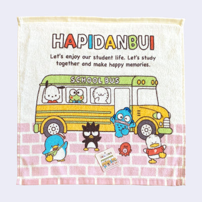 Cream colored hand towel with a printed illustration of Sanrio characters on and around a school bus, with text that reads "HAPIDANBUI - Let's enjoy our student life. Let's study together and make happy memories."