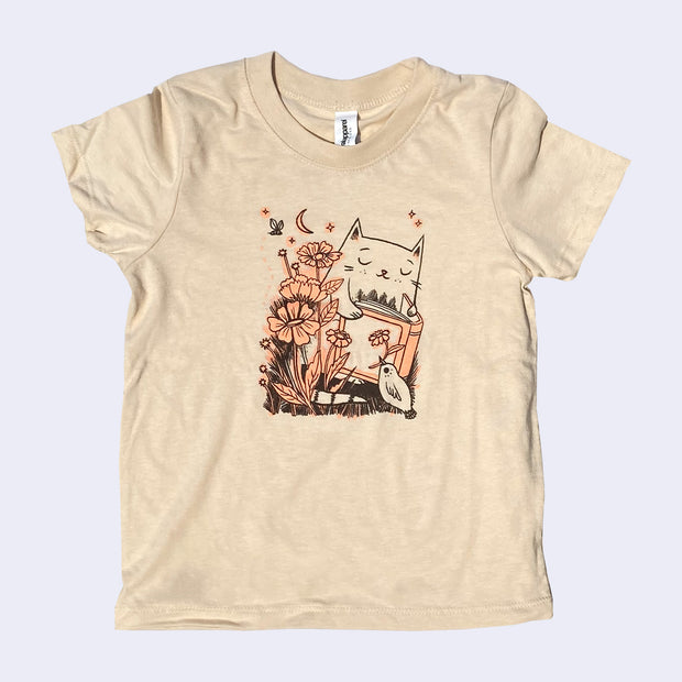 Tan children's t-shirt with an illustration of a cat reading a book with flowers and a small bird holding a flower in its beak.