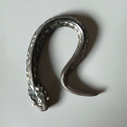 Ceramic sculpture of a dark gray snake with light silver eyes and imprinted scales along its body. Its tail curves slightly inward towards its head.