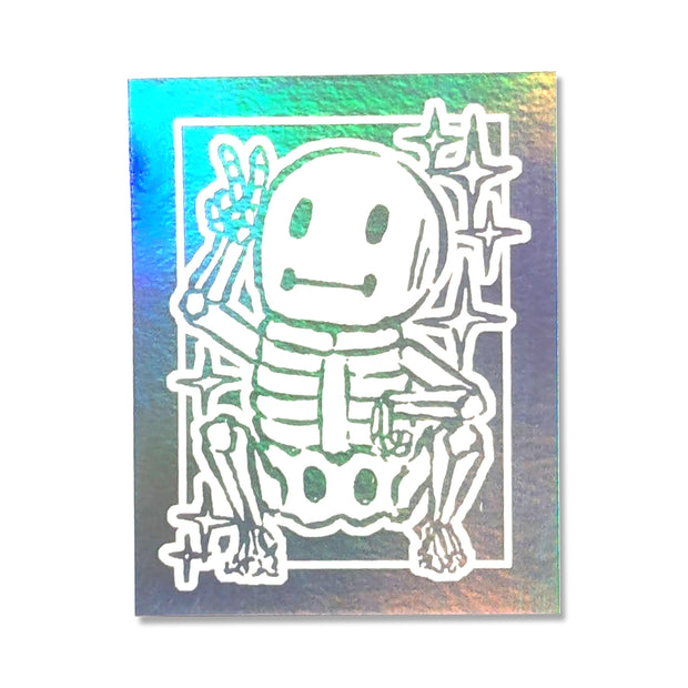 White ink sticker on holographic backing of a small cartoon skeleton, crouching and throwing up a peace sign.