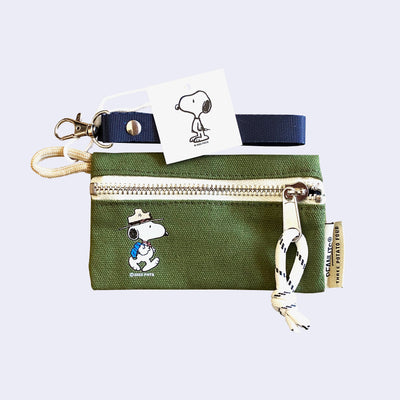 Small green canvas pouch with a zip closure, featuring a small illustration in the left corner of Snoopy wearing his hiking gear - a green hat and a blue backpack. It is attached to a blue fabric lanyard.