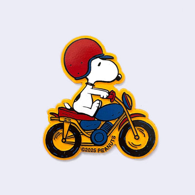 Die cut dimensional magnet of Snoopy riding atop a blue and red motorcycle, wearing a red retro looking half helmet. The border and background of the magnet is a bright yellow.