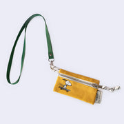 Small yellow canvas pouch with a zip closure, featuring a small illustration in the left corner of riding on a skateboard, going fast with speed lines behind him. It is attached to a green fabric lanyard.