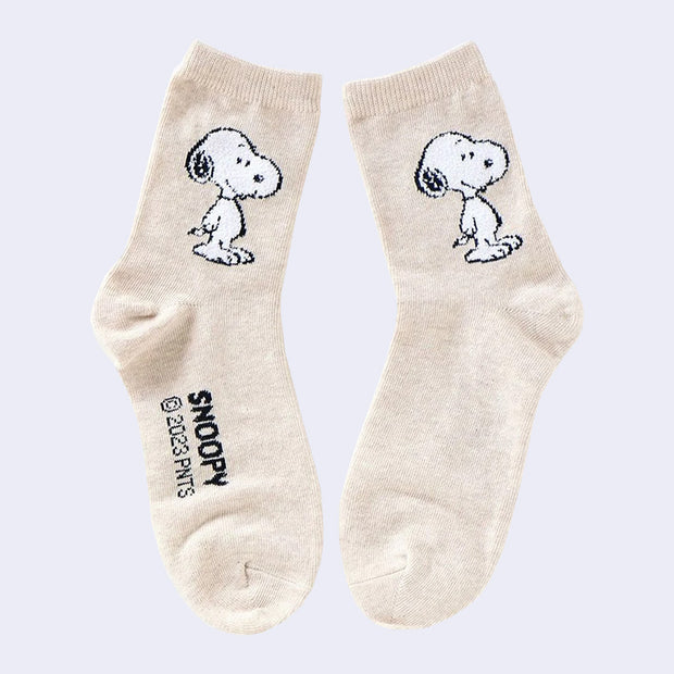 Beige colored socks with a graphic of Snoopy on the side, standing with his arms at his waist and smiling.