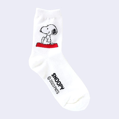 White crew socks with a graphic of Snoopy, sitting and smiling atop of his red dog house on the side of the sock. Only the top part of the dog house is seen.