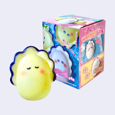 Small soft looking figure of a yellow cute cartoon oyster. It has a blue lining around it with closed eyes and rosy cheeks. It stands in front of its product packaging.