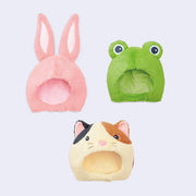 3 hood hats with fluffy outer lining, one of a pink rabbit, the other of a frog and the final of a calico cat