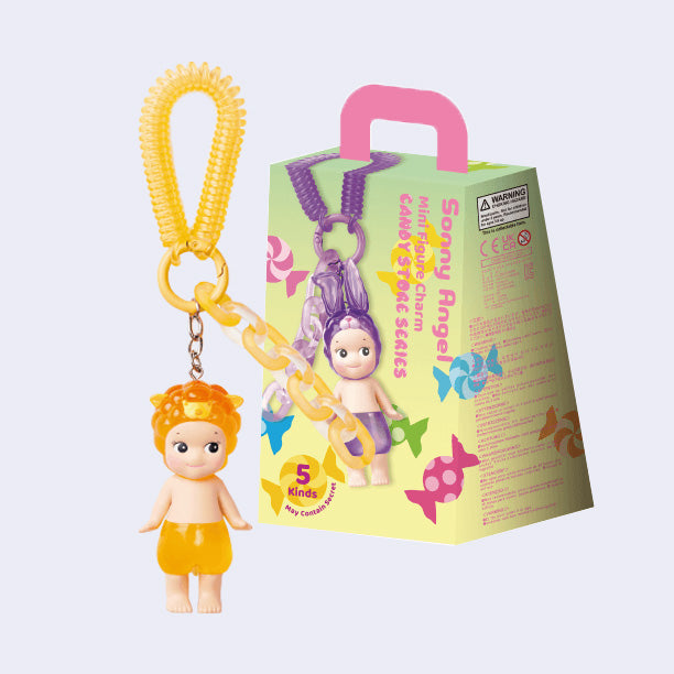 Mini figure of a Kewpie baby nude aside from a orange translucent shorts and a matching orange hood hat in the shape of a sheep. It is attached to an orange rubber chain, alongside decorative plastic chain. 