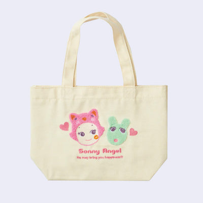 Cream colored canvas tote bag with a slightly shorter than normal strap. It has a fluffy embroidery on the front of a Sonny Angel's head, wearing a pink cat head hood hat. It has a kiss mark on its cheek and looks at a mint green Robby head, a cute mouse creature. Text under reads "Sonny Angel - He may bring you happiness!"