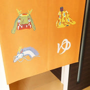 Close up of tapestry detail, orange with illustrated icons from Spirited Away, such as characters and symbols.