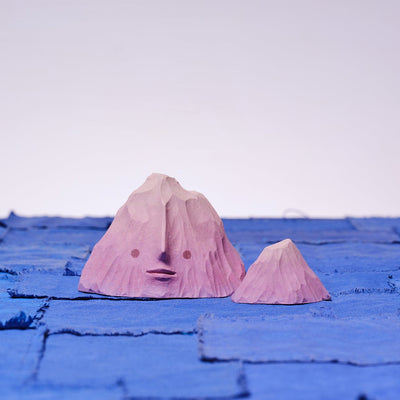 Set of 2 carved wooden sculptures, painted purple, of mountain ranges. One has an opened eye, slight smile facial expression and the other is without a face and smaller in size.