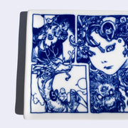 Rectangular shaped white porcelain plate with dark blue line art illustrations, depicting a woman with miniature lion like creatures on her shoulder and under her face. She looks at the viewer with a serious expression. To the left are illustrated panels of a person riding a dragon and another person creating a laser with their fingers. Close up.