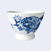 White ceramic bowl with a large rounded base that extends out slightly. A dark blue line illustration of a bird is on the bowl, it wears goggles and holds a stemmed flower in its mouth. The flower bud is like a spiked ball.