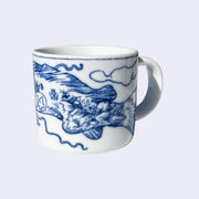 White porcelain mug with a dark blue line art illustration wrapped around it. A large koi fish with the number "14" on its side swims over a curling ocean wave.