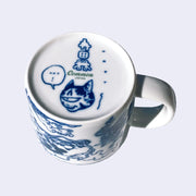 Underside of white porcelain mug, with a graphic of a one eyed stripe cat head with a speech bubble that reads "hot!"