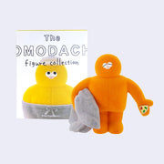 Flocked figure of an orange character with a round head and smooth tall and wide body, It has a closed eye expression, holds a gray blanket in one hand and a slice of pizza in the palm of the other.