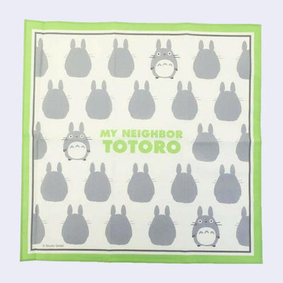 Cream colored handkerchief with a thick green border featuring a repeating pattern of small, gray chibi Totoros with "My Neighbor Totoro" written in the center in bold green font.