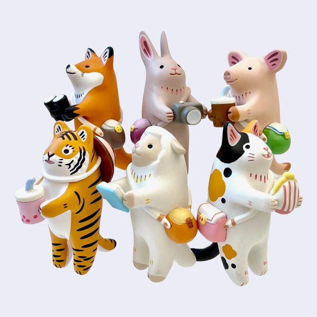 6 different animal figures standing on their hind legs, all with cross body bags and holding a different object such as: camera, binoculars, drink, book or coin pouch.