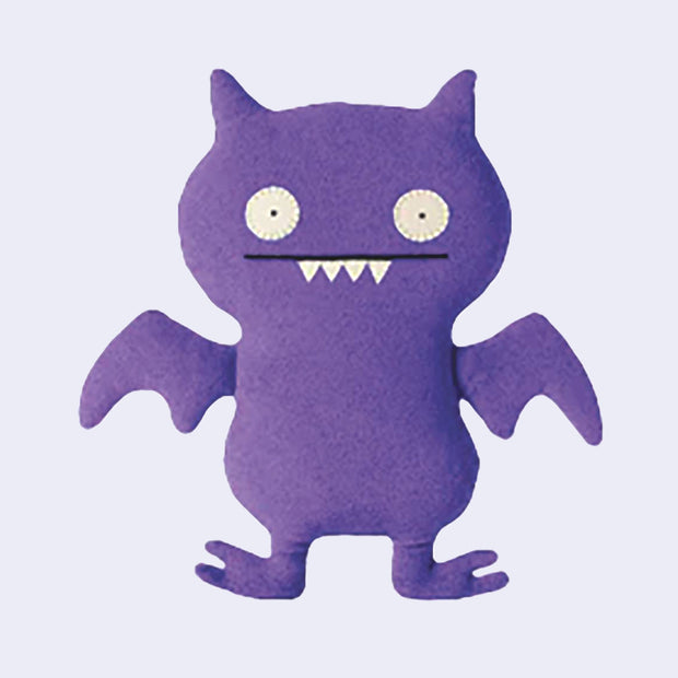 Purple plush monster doll, mostly flat in shape, with sewn on eyes and a straight mouth smile with 5 sharp pointed teeth.