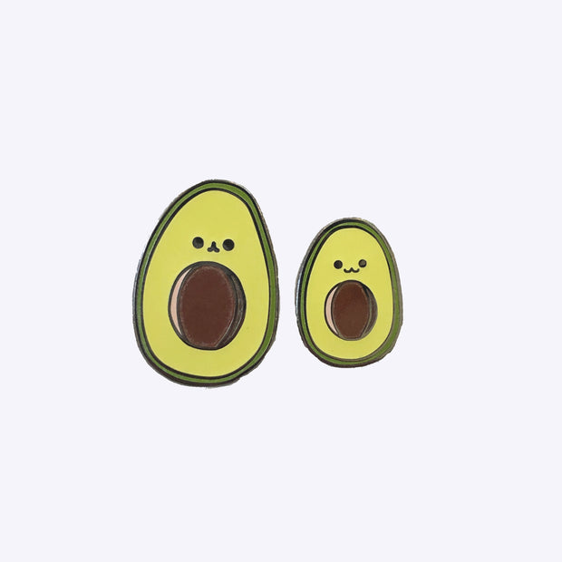 Two enamel pins of illustrated avocados with smiling faces, one is slightly smaller than the other.