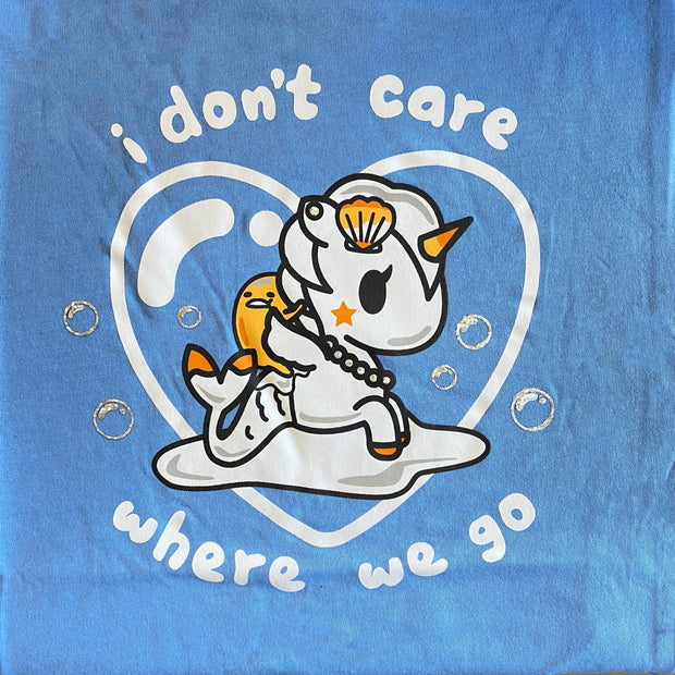 Close up of illustration. Gudetama riding a Mermicorno surrounded by a heart shaped bubble. White text says I don't care where we go. 