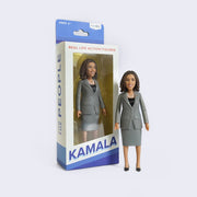 Action figure of politician Kamala Harris, wearing a gray blazer and matching skirt with black heels and a double pearl necklace. She smiles warmly.