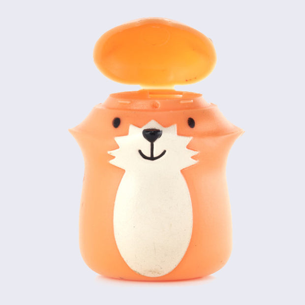 Plastic figure of a smiling orange cartoon fox with a happy face and a cream colored under body. Its head can be lifted up and floss can go inside.