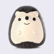 Plastic figure of a smiling brown cartoon hedgehog with a happy face and a cream colored under body. Its head can be lifted up and floss can go inside.