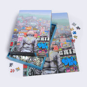 Puzzle is of an astronaut, faced away from the viewer and only visible from the waist up looking at mounts of graffiti'd containers and buildings.