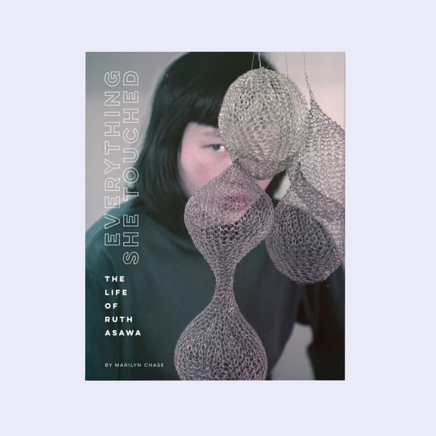 Book cover for Everything She Touched featuring a photo of artist Ruth Asawa standing behind some of her wire sculptures, modeled as rounded shapes.