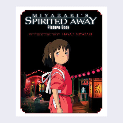 "Spirited Away Picture Book Cover" featuring an illustration from the movie. A girl stands in the center looking back over her shoulder with a serious expression. Behind her is a night setting of a rural town with red lights strung around it and buildings illuminated.