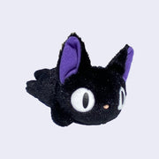 Small black plush cat with large eyes and purple ears, laying flat on its belly.