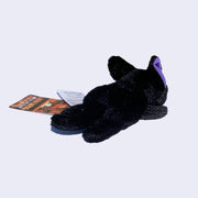 Small black plush cat with large eyes and purple ears, laying flat on its belly.