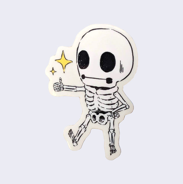 Small sticker of a black line art illustrated skeleton with a very large head, holding its arm out in a thumbs up position. Two yellow sparkles are above its thumb.