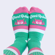 The front view of model wearing striped socks. The sock is mint but has stripes of pink and white. White cursive text near toes says giant robot.