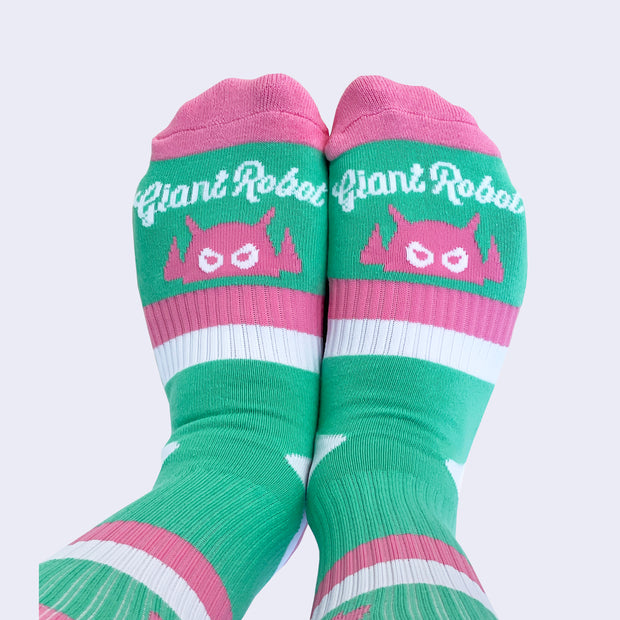 The front view of model wearing striped socks. The sock is mint but has stripes of pink and white. White cursive text near toes says giant robot.