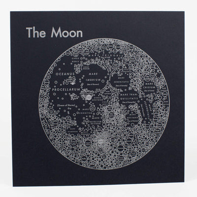 Silver letterpress on black paper of the moon, depicted abstractly as various circles, representing craters and geographical elements, written across the planet, aligned in relation to their real location. "The Moon" is written largely in the top left.