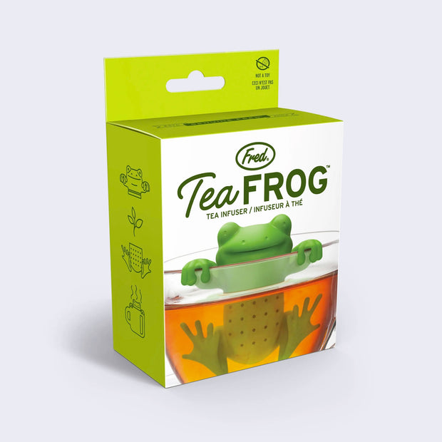 Product packaging, white box with green border and photo of a silicone green frog shaped tea infuser inside of a clear mug with tea inside of it. Text says "Tea Frog tea infuser"