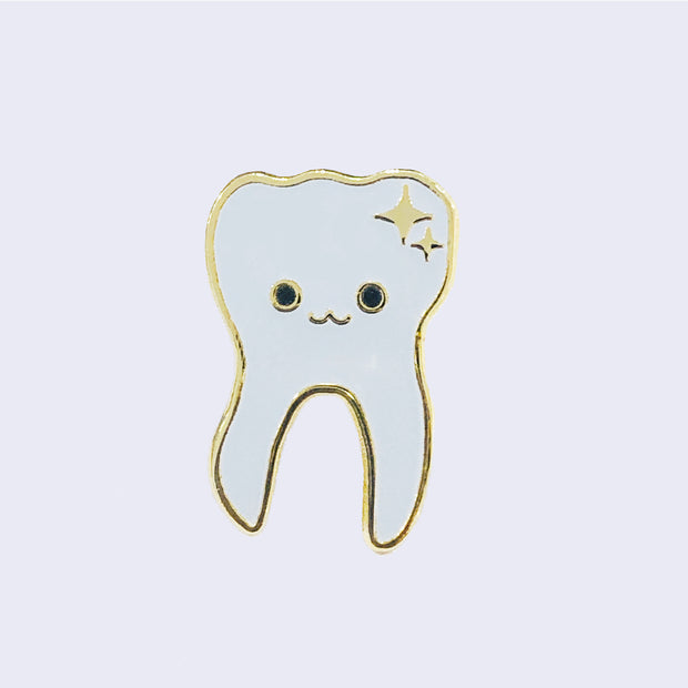 Enamel pin of an illustrated smiling white tooth with gold sparkles in the top right corner and a gold outline.