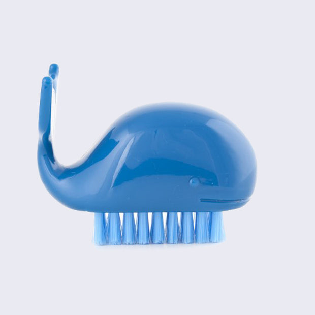 Dark blue plastic cartoon whale, with a semi circle bodies and a wide tail curved upward. It has a soft bristled brush attached to its underside, for brushing nails or cleaning hands