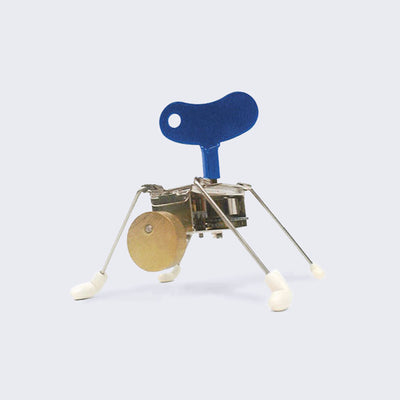 Small robotic toy with a rectangular body, 4 thin wire legs with white boots on each. A large blue crank is attached to its main body and it has a small circle for a head.